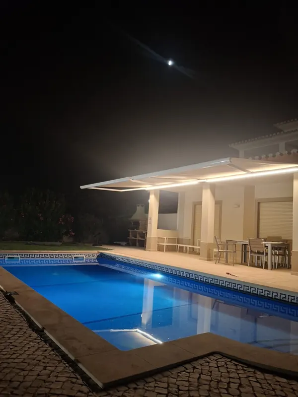 Motorised awning lit at night by the pool